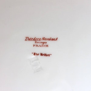May include: A white porcelain plate with a red inscription that reads "Theodore Haviland Limoges France" and "The Belfort".