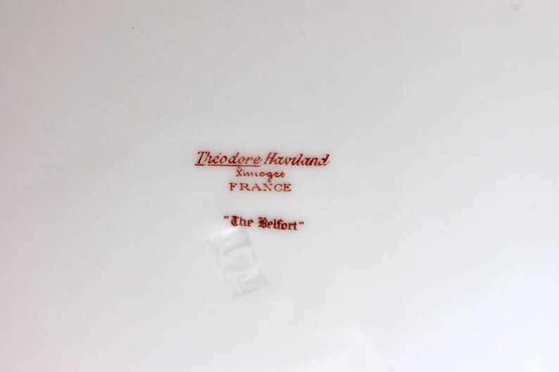 May include: A white porcelain plate with a red inscription that reads "Theodore Haviland Limoges France" and "The Belfort".