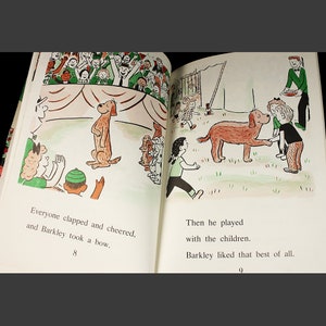 May include: A brown dog stands on its hind legs on a stage with a red and white striped tent. The dog is surrounded by a crowd of people clapping and cheering. The text "Everyone clapped and cheered, and Barkley took a bow." is printed below the image.