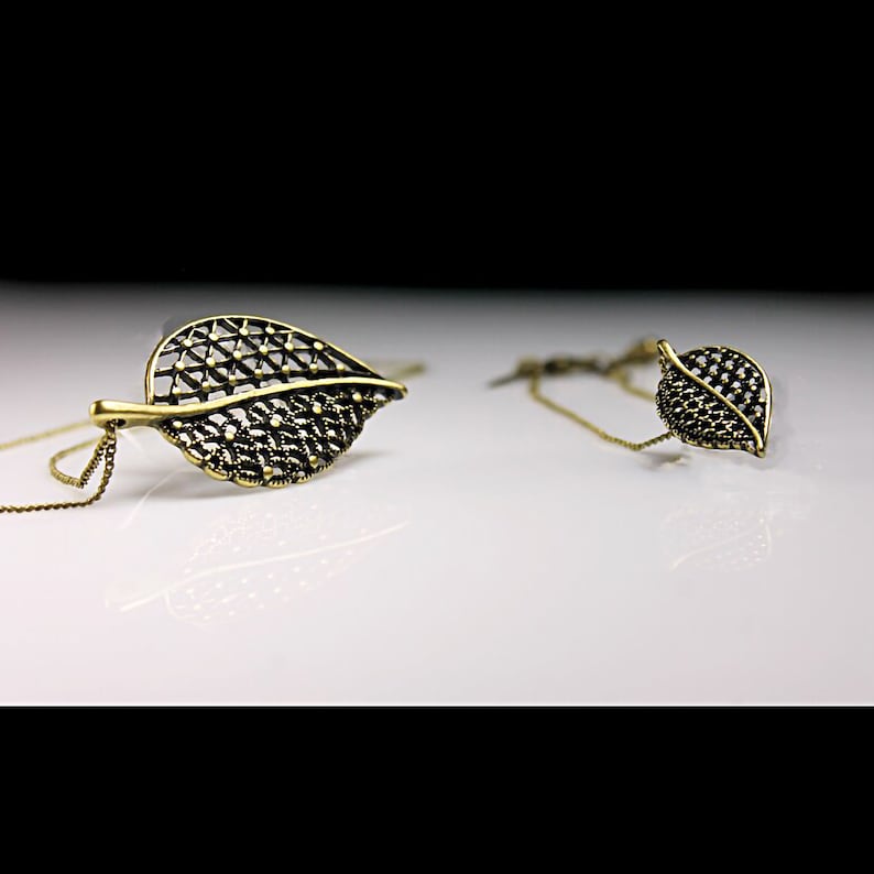 May include: Two gold leaf-shaped necklaces with intricate designs. The larger necklace has a chain, while the smaller necklace has a shorter chain.