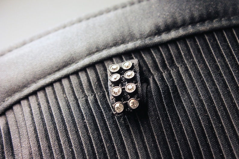 May include: A black fabric with a silver and black embellishment featuring a row of clear rhinestones.