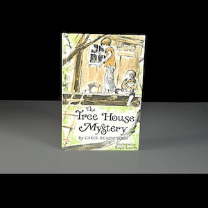 May include: A children's book titled "The Tree House Mystery" by Carol Beach York, illustrated by Reisie Lonette. The cover shows an illustration of two children near a treehouse, with a ladder and wooden structure.