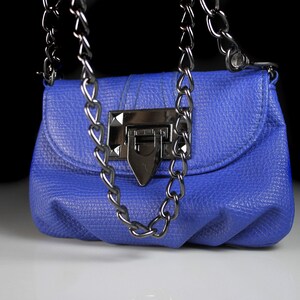 Pode incluir: Uma pequena bolsa azul cobalto com um acabamento texturizado. A bolsa apresenta uma al&ccedil;a de corrente prateada e um fecho de encaixe a condizer. O design &eacute; simples e elegante, adequado para v&aacute;rias ocasi&otilde;es.