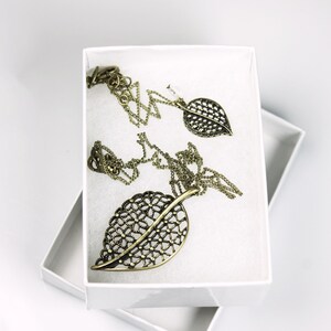 May include: A set of gold leaf-shaped jewelry, including a necklace and earrings, displayed in a white box.