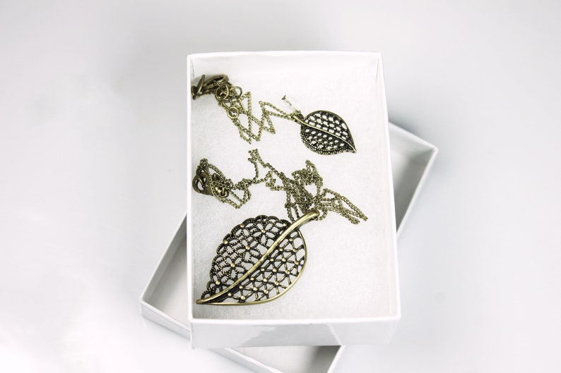 May include: A set of gold leaf-shaped jewelry, including a necklace and earrings, displayed in a white box.