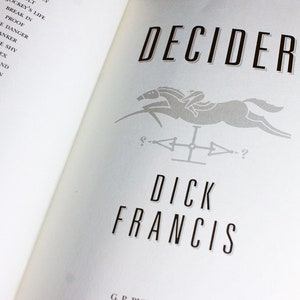 May include: A book cover with the title "Decider" in black text. The cover features a gray silhouette of a horse and rider jumping over a fence. The author's name, "Dick Francis", is printed in black below the image.