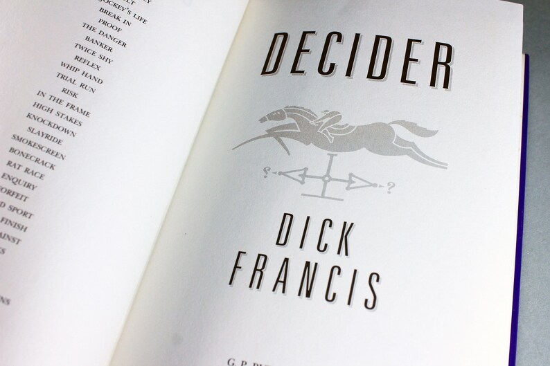 May include: A book cover with the title "Decider" in black text. The cover features a gray silhouette of a horse and rider jumping over a fence. The author's name, "Dick Francis", is printed in black below the image.