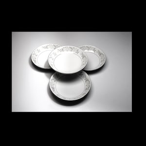 Puede incluir: Cuatro cuencos de cerámica blanca con un diseño floral plateado. Los cuencos están apilados uno encima del otro.