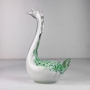 May include: A white glass swan figurine with green speckled accents. The swan has a long neck and a curved beak.