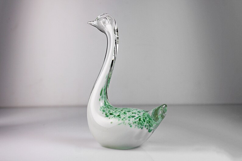 May include: A white glass swan figurine with green speckled accents. The swan has a long neck and a curved beak.