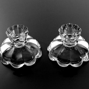 Puede incluir: Dos candelabros de vidrio transparente con borde festoneado y dise&ntilde;o acanalado. Los candelabros est&aacute;n sobre una superficie negra.