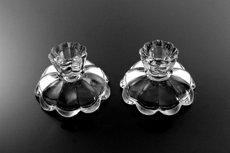 Puede incluir: Dos candelabros de vidrio transparente con borde festoneado y dise&ntilde;o acanalado. Los candelabros est&aacute;n sobre una superficie negra.