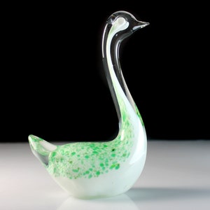 May include: A white glass swan figurine with green and white speckled accents. The swan has a long, curved neck and a small, round body.
