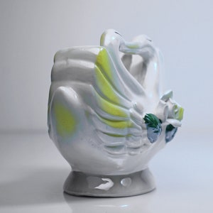 May include: White ceramic planter shaped like two swans with their necks intertwined. The swans have yellow and green accents and a floral design.