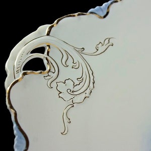 May include: Close-up of a white porcelain plate with a blue and white floral design. The plate has a scalloped edge and is decorated with gold trim. The design features a delicate floral pattern with a blue and white color scheme.