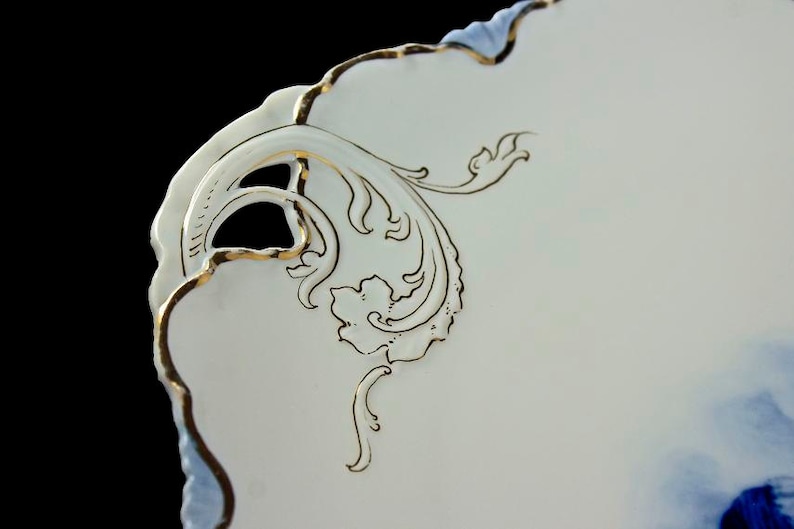 May include: Close-up of a white porcelain plate with a blue and white floral design. The plate has a scalloped edge and is decorated with gold trim. The design features a delicate floral pattern with a blue and white color scheme.
