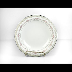 May include: White porcelain serving bowl with a delicate floral and lace design around the rim. The rim features a silver trim and a scalloped edge. The bowl is displayed on a decorative gold-toned metal stand.