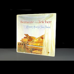 Puede incluir: Funda de disco de vinilo vintage con el texto "Ferrante and Teicher" en rojo y "Romantic Moods for Twin Pianos" en azul. La portada muestra dos pianos de cola dorados.