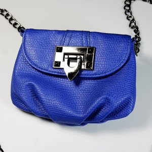 Pode incluir: Uma pequena bolsa azul cobalto com acabamento texturizado. A bolsa apresenta um fecho prateado e uma al&ccedil;a de corrente preta. A bolsa foi projetada para ser usada no ombro ou na transversal.