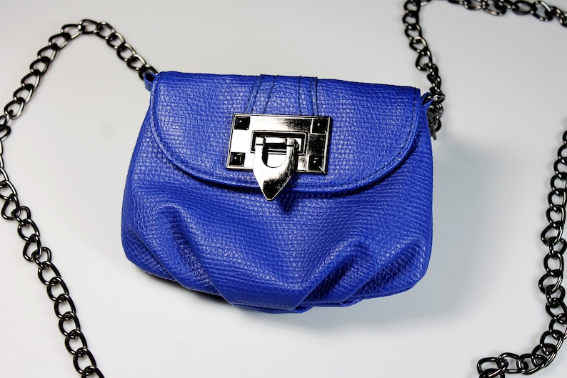 Pode incluir: Uma pequena bolsa azul cobalto com acabamento texturizado. A bolsa apresenta um fecho prateado e uma al&ccedil;a de corrente preta. A bolsa foi projetada para ser usada no ombro ou na transversal.
