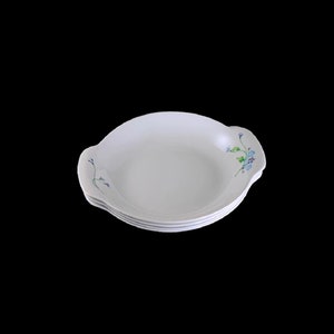 May include: A set of four white ceramic bowls with a floral design. The bowls have a rounded shape and a slightly flared rim. The floral design is in shades of blue and green.