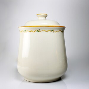 May include: White ceramic canister with a lid and a yellow and green ribbon design around the top.