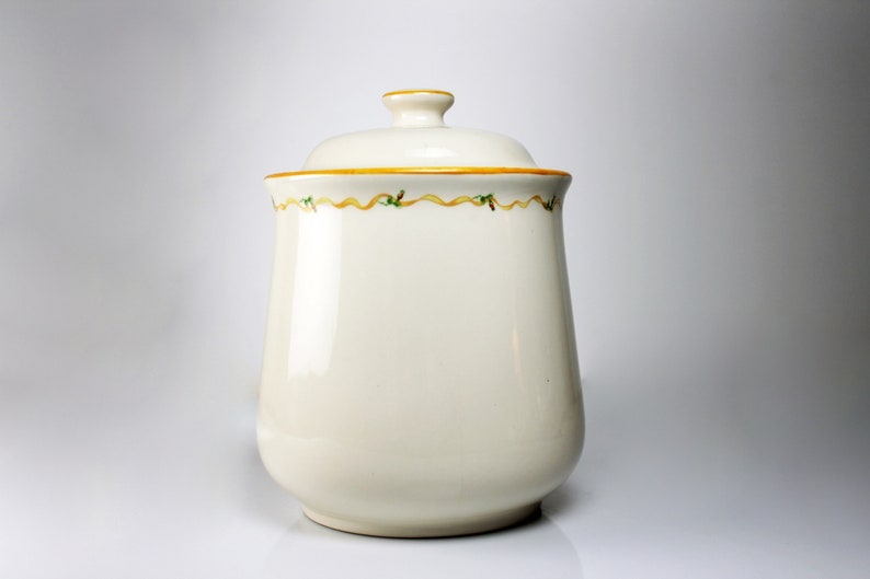 May include: White ceramic canister with a lid and a yellow and green ribbon design around the top.