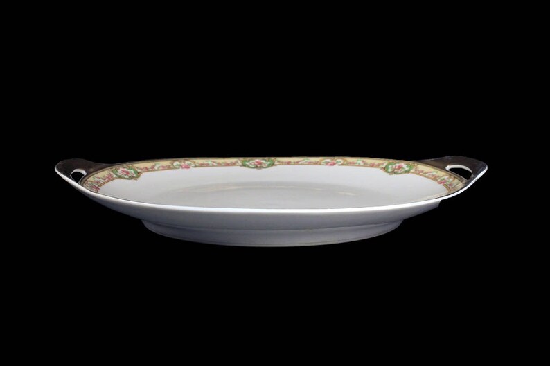 May include: A white oval serving platter with a floral design in shades of pink, green, and gold. The platter has two handles on the sides.