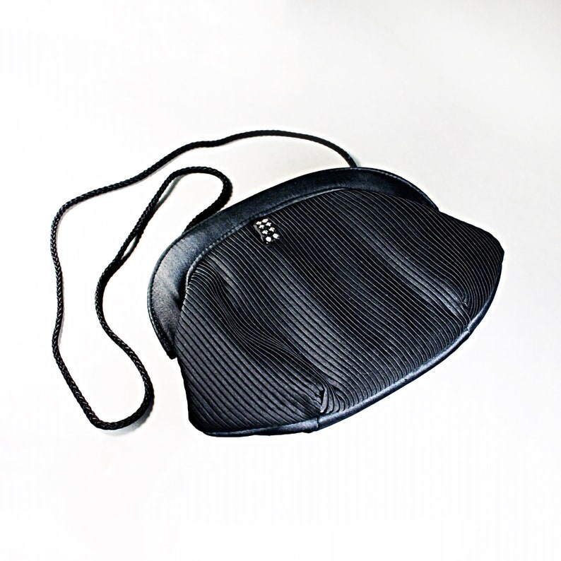 May include: A black pleated evening bag with a short strap and a small, sparkly embellishment.