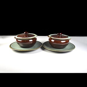 Peut inclure: Deux bols à soupe en céramique marron avec couvercles, chacun posé sur une soucoupe assortie. Les bols ont un bord vert clair et un couvercle marron foncé avec un petit bouton. Les soucoupes sont vert clair avec un bord marron. Fond noir et blanc.