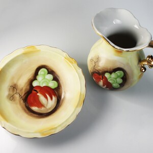 Puede incluir: Un juego de vajilla de cocina de cer&aacute;mica vintage con un dise&ntilde;o pintado a mano de frutas y uvas. El juego incluye un taz&oacute;n y una jarra con asa dorada.