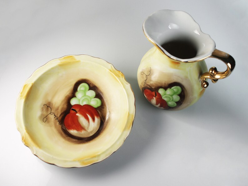 Puede incluir: Un juego de vajilla de cocina de cer&aacute;mica vintage con un dise&ntilde;o pintado a mano de frutas y uvas. El juego incluye un taz&oacute;n y una jarra con asa dorada.