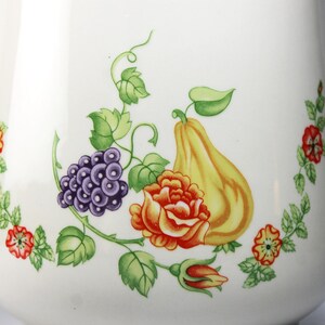May include: White ceramic pitcher with a floral design featuring a pear, grapes, and a rose. The design is in shades of green, purple, orange, and yellow.