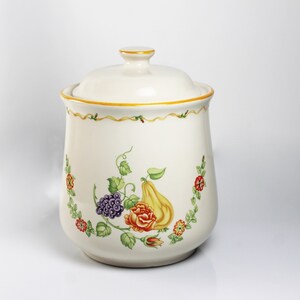 May include: White ceramic canister with a lid, featuring a floral design with a pear, grapes, and a rose. The design is in shades of green, yellow, red, purple, and brown.