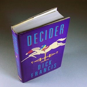 May include: A purple hardcover book with the title "DECIDER" in blue and red lettering. The cover features a white horse jumping over a fence with a rider in a blue and yellow outfit. The author's name, "DICK FRANCIS", is printed in blue lettering below the horse.