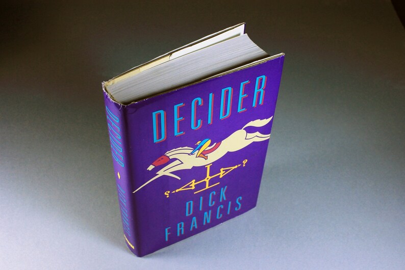 May include: A purple hardcover book with the title "DECIDER" in blue and red lettering. The cover features a white horse jumping over a fence with a rider in a blue and yellow outfit. The author's name, "DICK FRANCIS", is printed in blue lettering below the horse.
