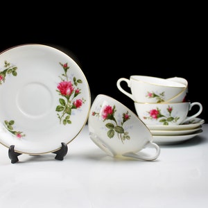 Peut inclure: Un ensemble de quatre tasses &agrave; th&eacute; et soucoupes blanches avec un motif floral repr&eacute;sentant des roses roses et des feuilles vertes. Les tasses et les soucoupes ont une bordure dor&eacute;e.
