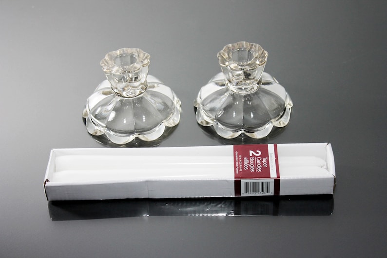 Puede incluir: Dos candelabros de vidrio transparente con borde festoneado y un paquete de dos velas de t&eacute; blancas. El paquete de velas dice "Taper Candles 2 Bougie edilles"