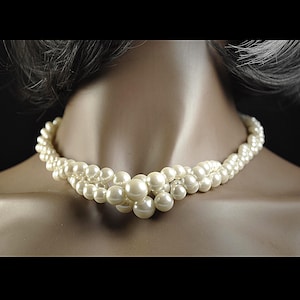 May include: A cream-coloured pearl necklace with multiple strands. The necklace is displayed on a mannequin and features a graduated design with larger pearls clustered at the centre.