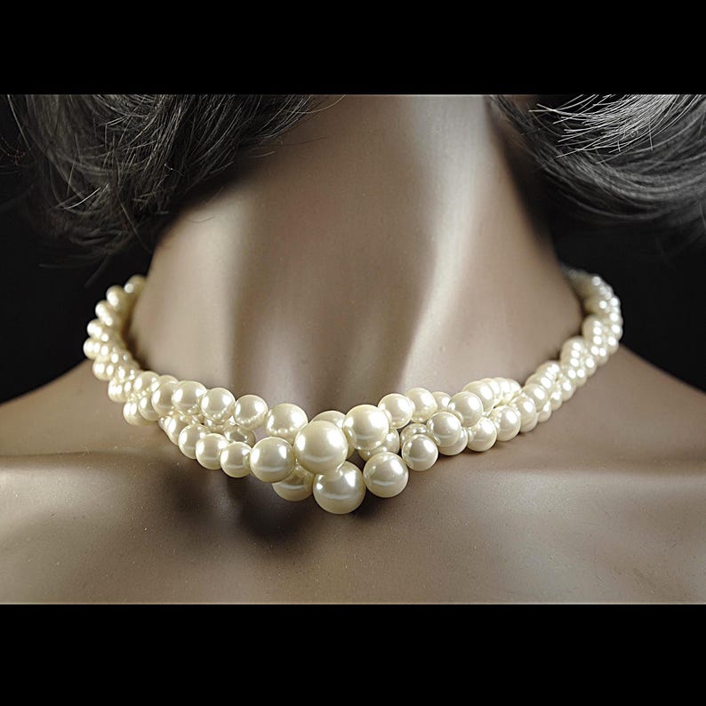 May include: A cream-coloured pearl necklace with multiple strands. The necklace is displayed on a mannequin and features a graduated design with larger pearls clustered at the centre.