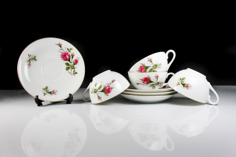 Peut inclure: Un ensemble de quatre tasses &agrave; th&eacute; et soucoupes blanches avec un motif floral compos&eacute; de roses roses et de feuilles vertes. Les tasses et les soucoupes sont empil&eacute;es les unes sur les autres.
