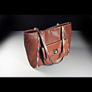 May include: A brown leather tote bag with a snakeskin patterned strap. The bag has a front pocket and a silver accent.