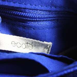 Pode incluir: Close-up do interior de uma bolsa azul cobalto com z&iacute;per a condizer e uma etiqueta branca. A etiqueta diz "ecote" em uma fonte simples em min&uacute;sculas. O tecido da bolsa tem uma apar&ecirc;ncia texturizada.