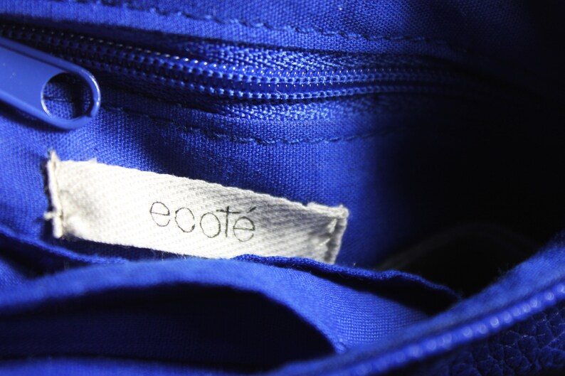 Pode incluir: Close-up do interior de uma bolsa azul cobalto com z&iacute;per a condizer e uma etiqueta branca. A etiqueta diz "ecote" em uma fonte simples em min&uacute;sculas. O tecido da bolsa tem uma apar&ecirc;ncia texturizada.