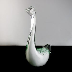 May include: A white glass swan figurine with green speckles throughout. The swan has a long neck and a curved body.