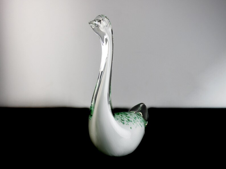 May include: A white glass swan figurine with green speckles throughout. The swan has a long neck and a curved body.