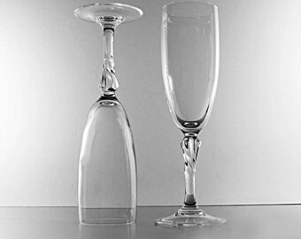 May include: Two clear champagne flutes. One is upright, the other is inverted. Both have a twisted stem design. The glasses are on a reflective surface, with a gradient background.