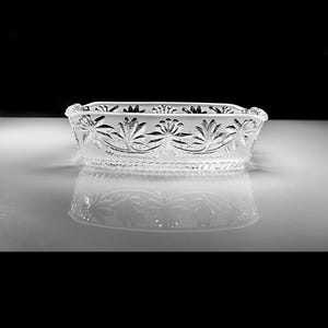May include: A clear, rectangular glass dish with a floral design etched around the rim. The dish is reflected on a white surface, creating a symmetrical image. The design features stylized flowers and leaves.