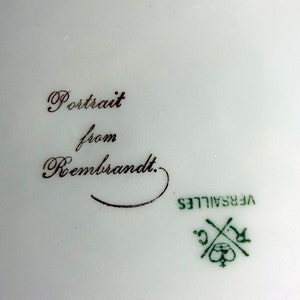 May include: Close-up of a white porcelain plate with a black inscription that reads "Portrait from Rembrandt." The plate also has a green mark that reads "VERSAILLES C."