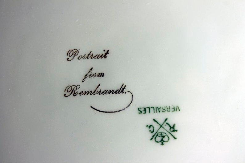 May include: Close-up of a white porcelain plate with a black inscription that reads "Portrait from Rembrandt." The plate also has a green mark that reads "VERSAILLES C."